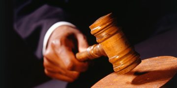 Close up of a wooden gavel strucking a wooden block by a hand.